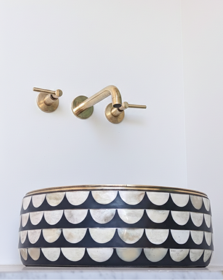 Black and white patterned sink with gold faucet against a white wall
