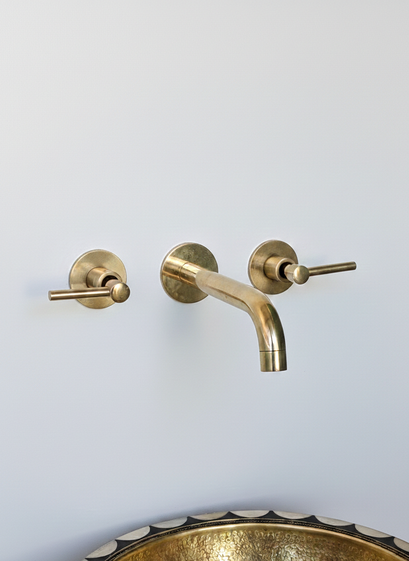 Brass wall-mounted faucet set on a white wall with a decorative copper sink below.