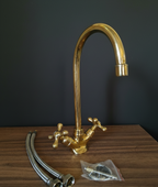 Gold kitchen faucet with hoses and connectors on a wooden surface against a dark background