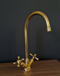 Gold kitchen faucet on a wooden surface with a dark background
