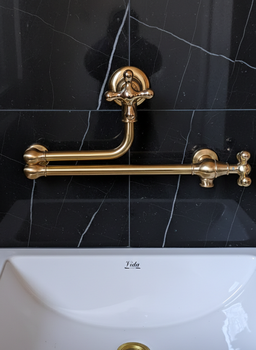 brass pot filler on a black tiled wall with a white sink below.