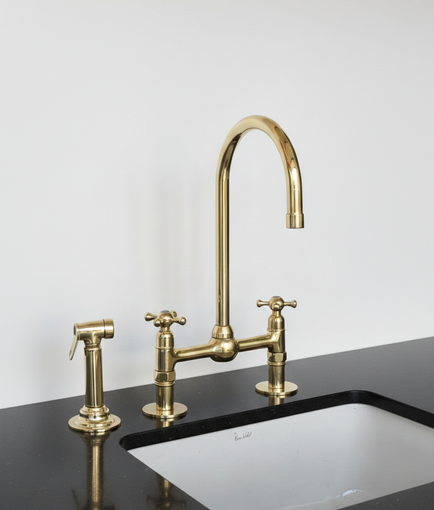 Brass kitchen faucet and handles on a black countertop with a white wall background