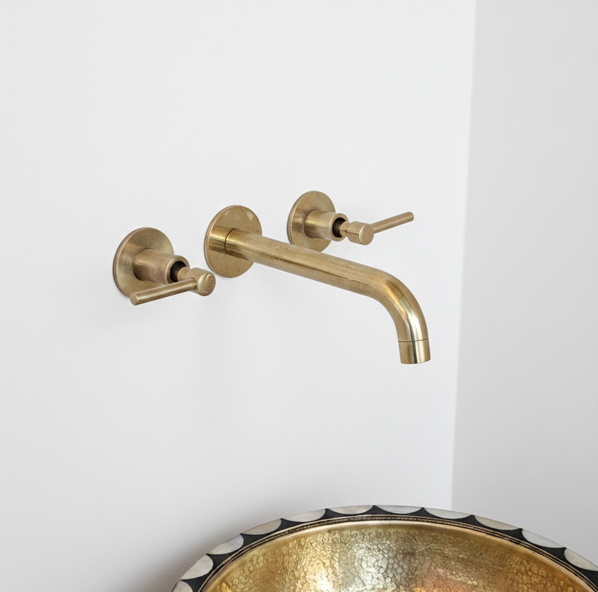 Gold wall-mounted faucet on a white wall with a decorative gold sink.