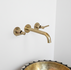 Gold wall-mounted faucet on a white wall with a decorative gold sink.